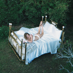 Woman lying on a bed outdoors with greenery around